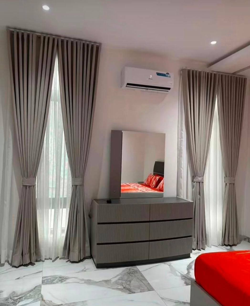 A bedroom with a mirrored dresser set between floor to ceiling curtains
